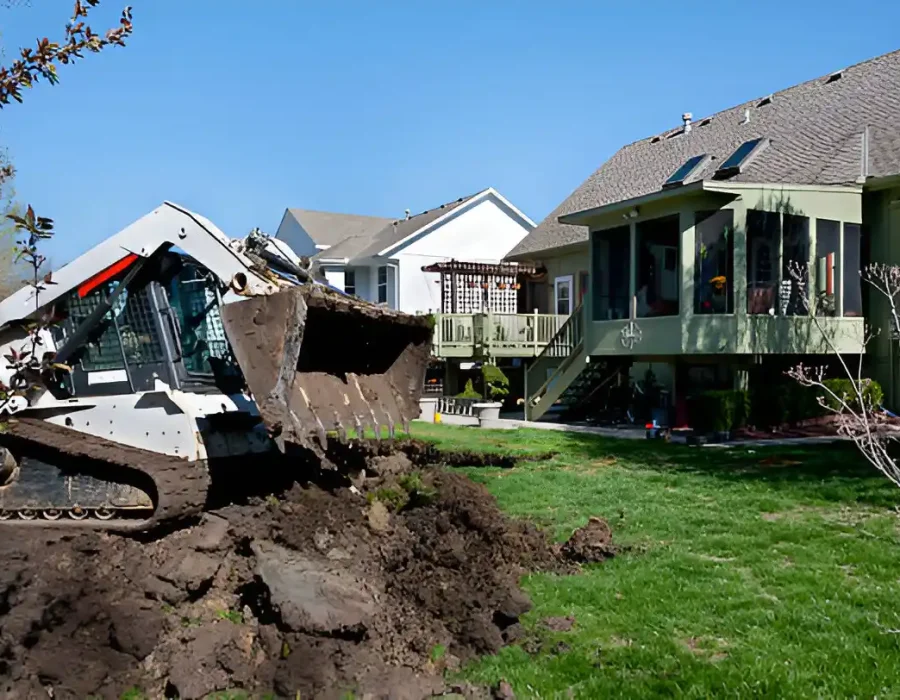 Skid steer loader performing soil excavation and site prep in residential backyard demolition