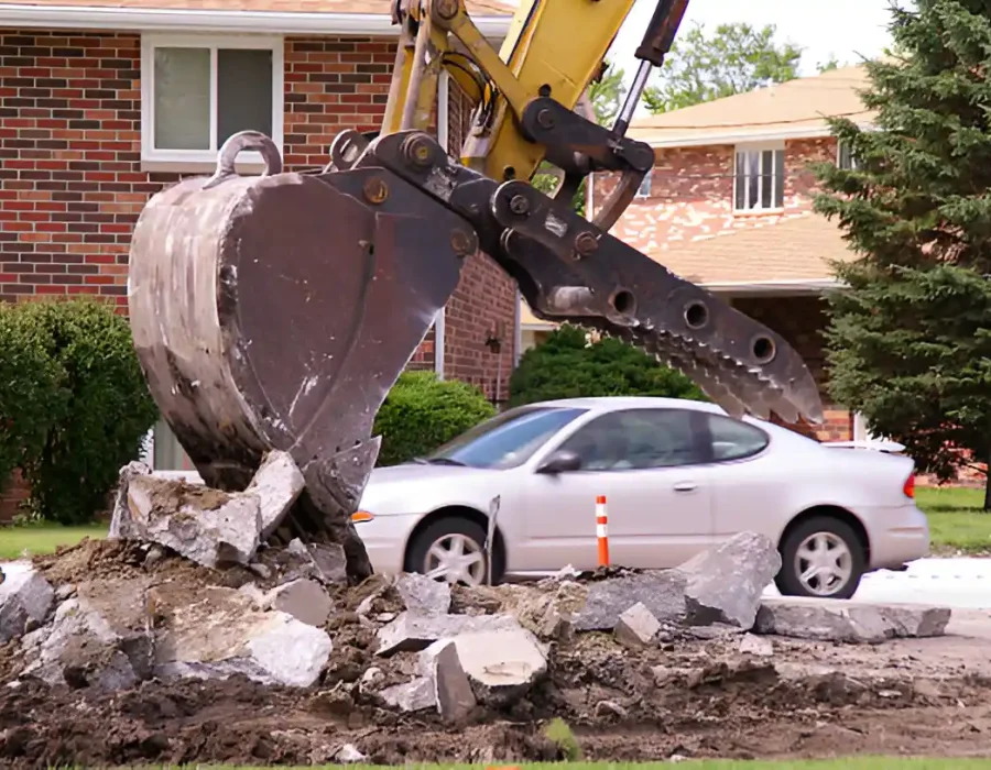 Heavy-duty excavator bucket demolishing concrete driveway at suburban residential property