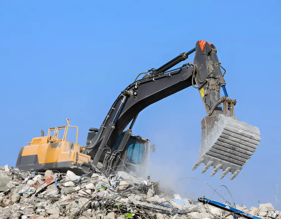 Industrial excavator with bucket sorting demolition debris against blue sky at construction site