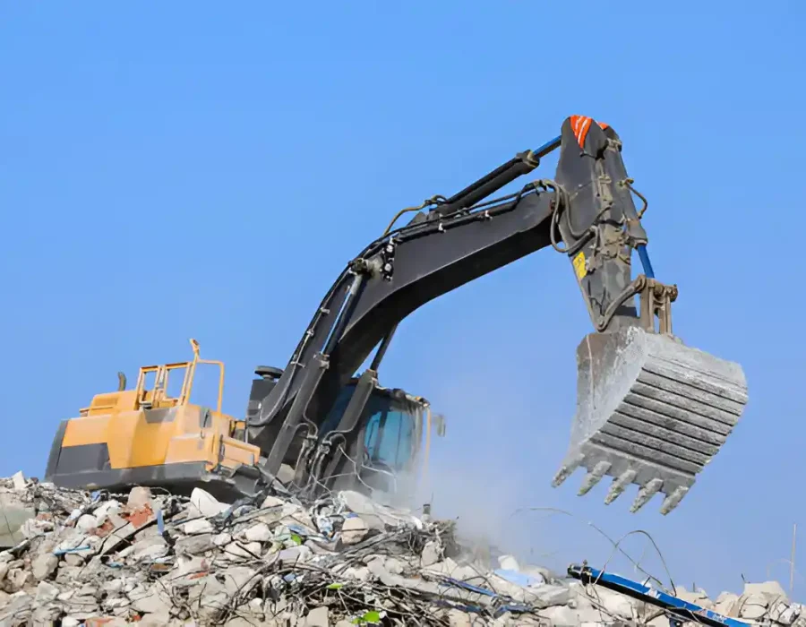Large excavator with bucket clearing concrete debris at commercial building demolition site