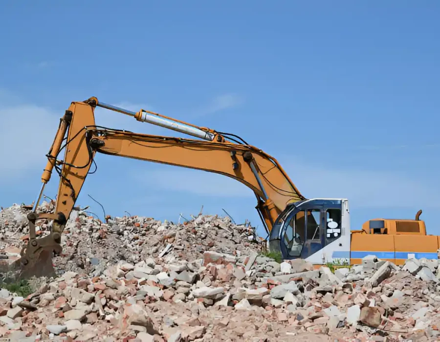Yellow excavator sorting through brick and concrete debris at large-scale demolition site
