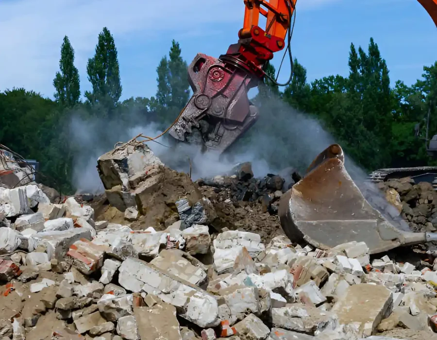 Heavy-duty demolition crusher attachment pulverizing concrete debris with dust cloud at work site