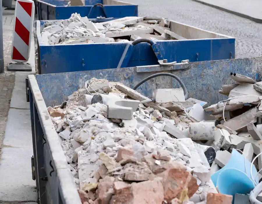 Blue industrial dumpsters loaded with mixed demolition waste and concrete rubble on urban street