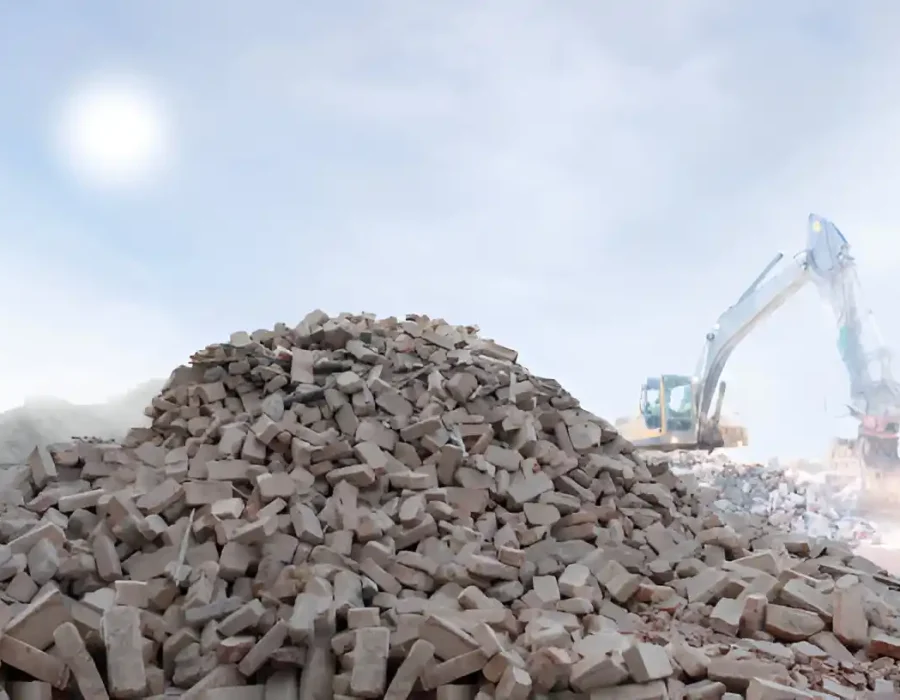 Massive pile of crushed concrete with excavator working in background against bright sky