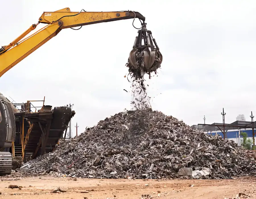 Yellow excavator with grapple attachment dumping debris onto sorted demolition waste pile