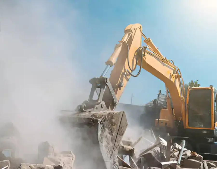 Yellow excavator with bucket breaking through concrete structure amid demolition dust cloud
