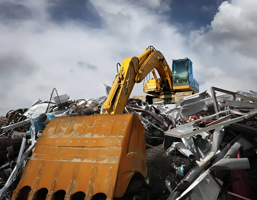 Excavator with bucket among piles of sorted metal debris at industrial demolition facility