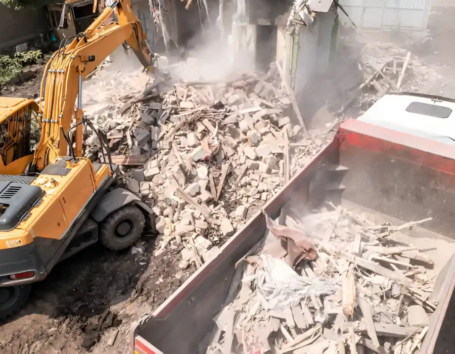 Excavator and dump truck removing demolished building materials during structural teardown
