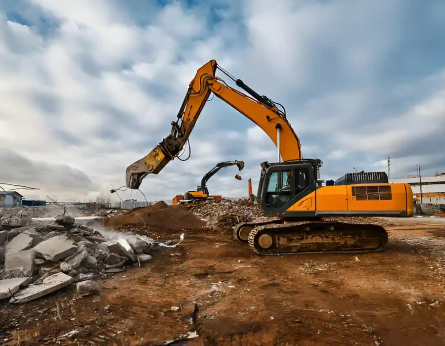 Two yellow excavators clearing construction debris at demolition site under cloudy sky