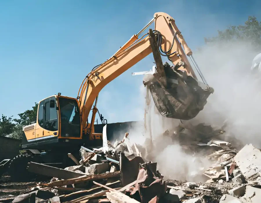 Yellow excavator with bucket demolishing building amid dust clouds on sunny worksite