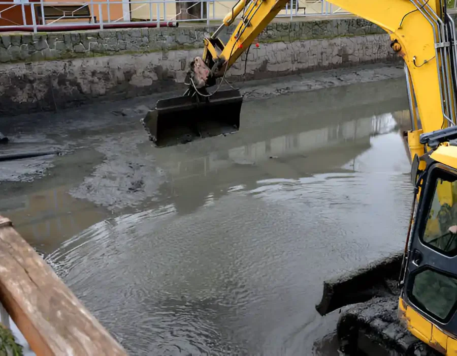 Excavator clearing muddy water and debris during removal project.