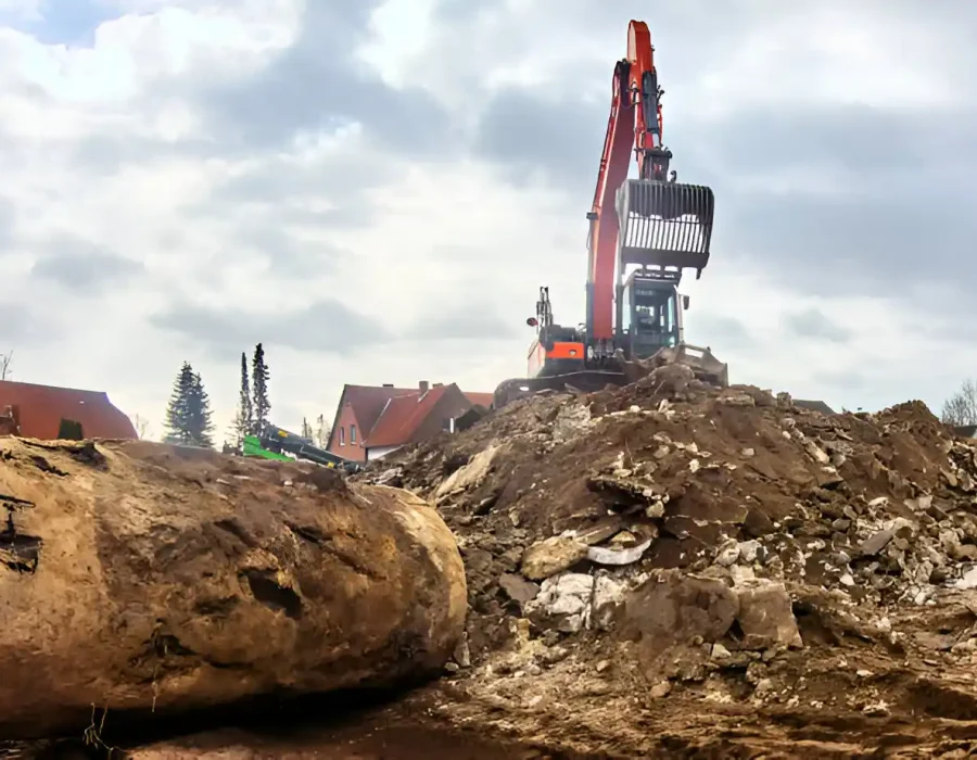Orange excavator managing debris on demolition site, large rocks and soil in background