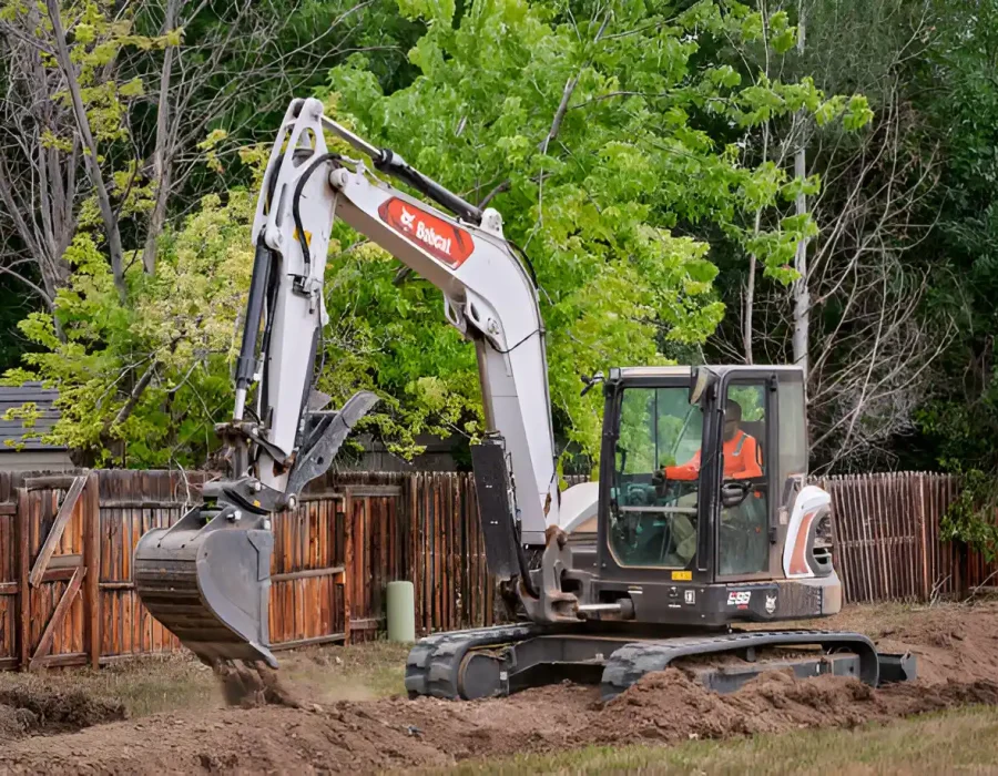Excavator digging in yard, preparing land for landscaping or site cleanup, trees in background