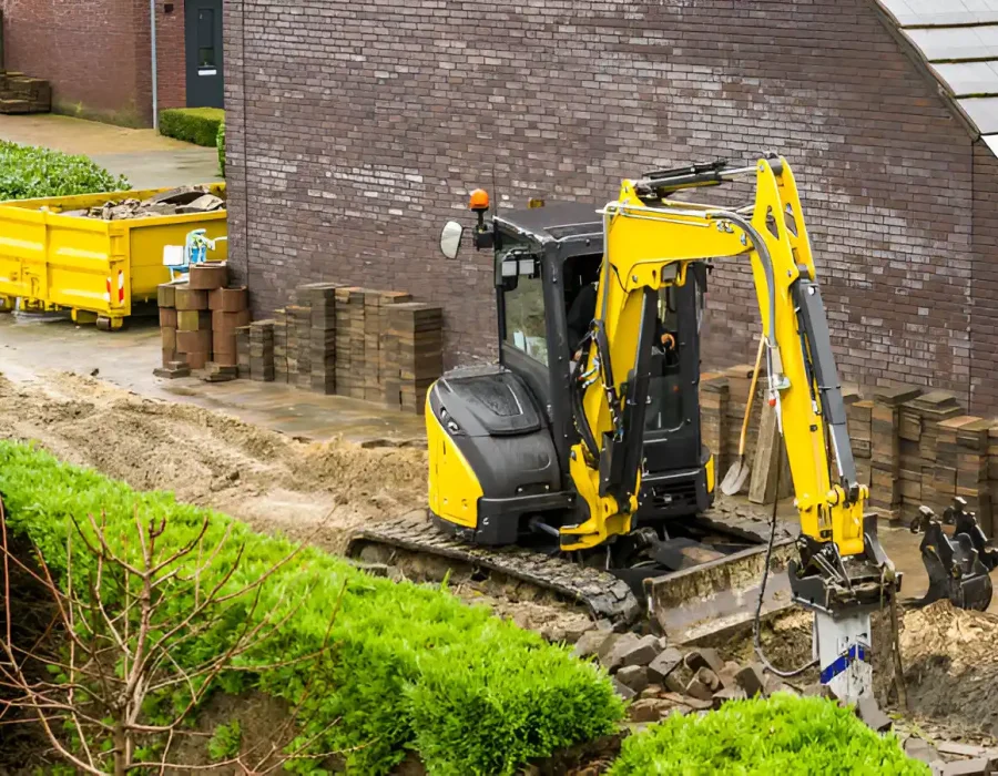 Yellow excavator digging on site, debris removal with waste container and bricks stacked nearby