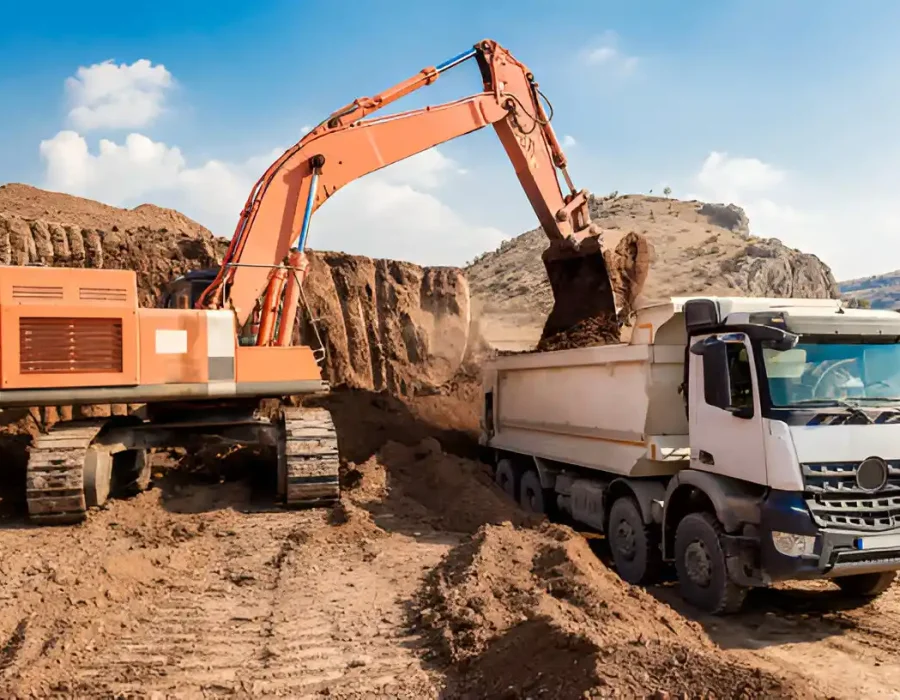 Excavator transferring soil into white dump truck, debris removal and site preparation in progress