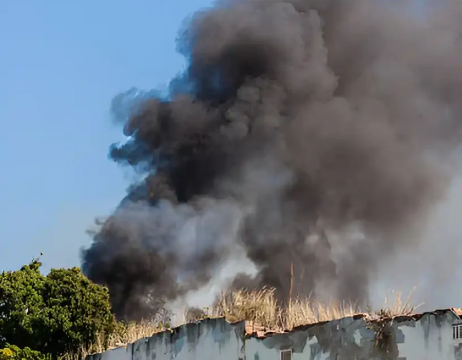 Thick black smoke rising from a demolished building site, indicating cleanup operations