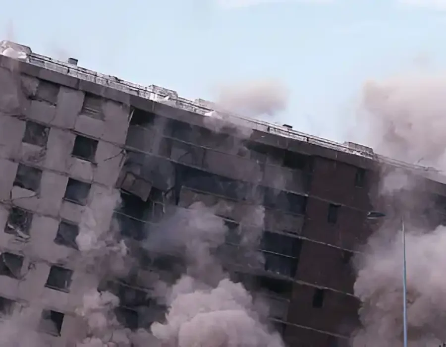 Multi-story building collapsing with dust and debris, indicating professional demolition in action.