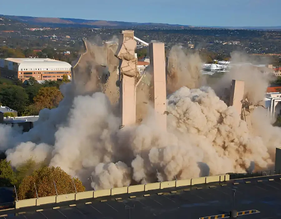 Building demolition in progress with large dust cloud, indicating debris removal and site preparation.