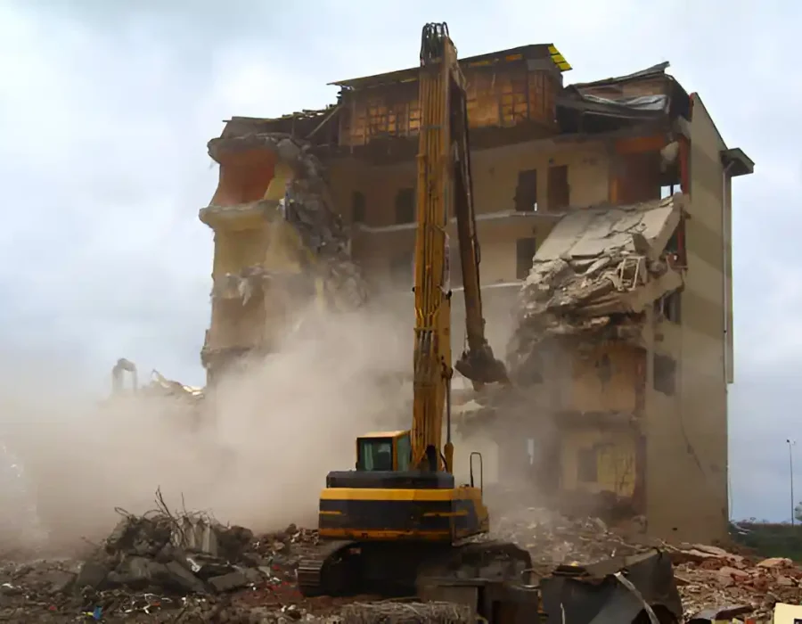 Excavator demolishing a building, with debris and dust cloud indicating site cleanup and removal services.