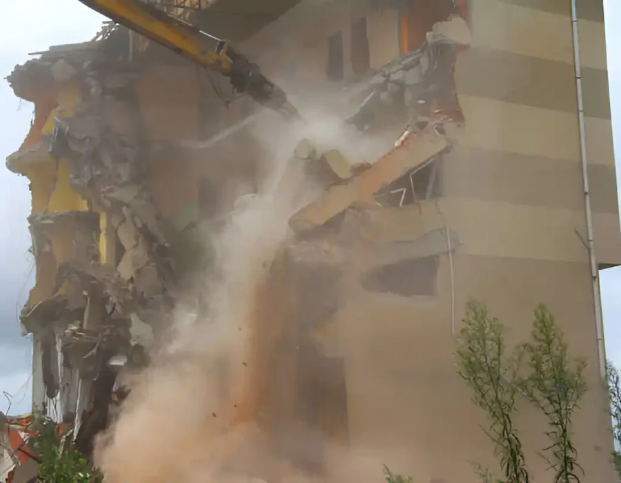 Excavator arm demolishing apartment building with water spray system controlling dust spread