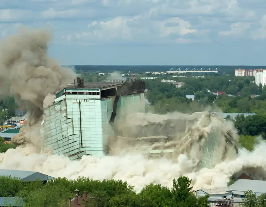 Controlled building collapse with massive dust cloud in urban landscape, professional removal