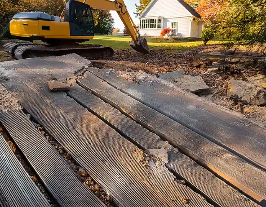 Yellow excavator performing demolition and site clearing near house with exposed ground materials and debris