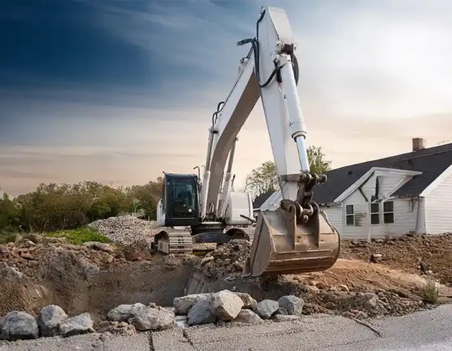 Large excavator conducting residential demolition and debris removal with house in background