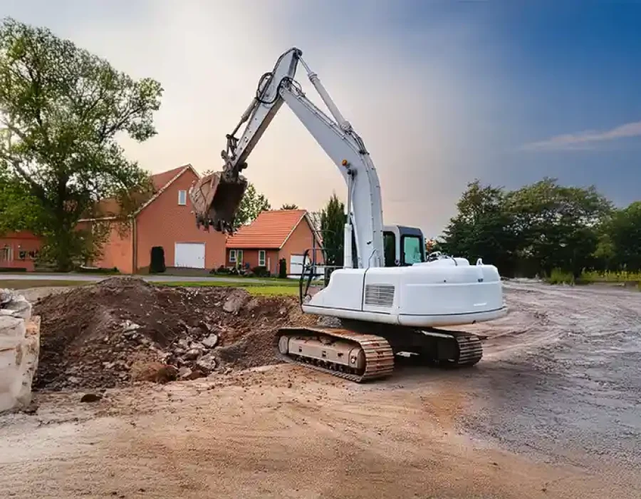 Heavy-duty excavator performing residential site preparation with demolition equipment near coral-colored houses