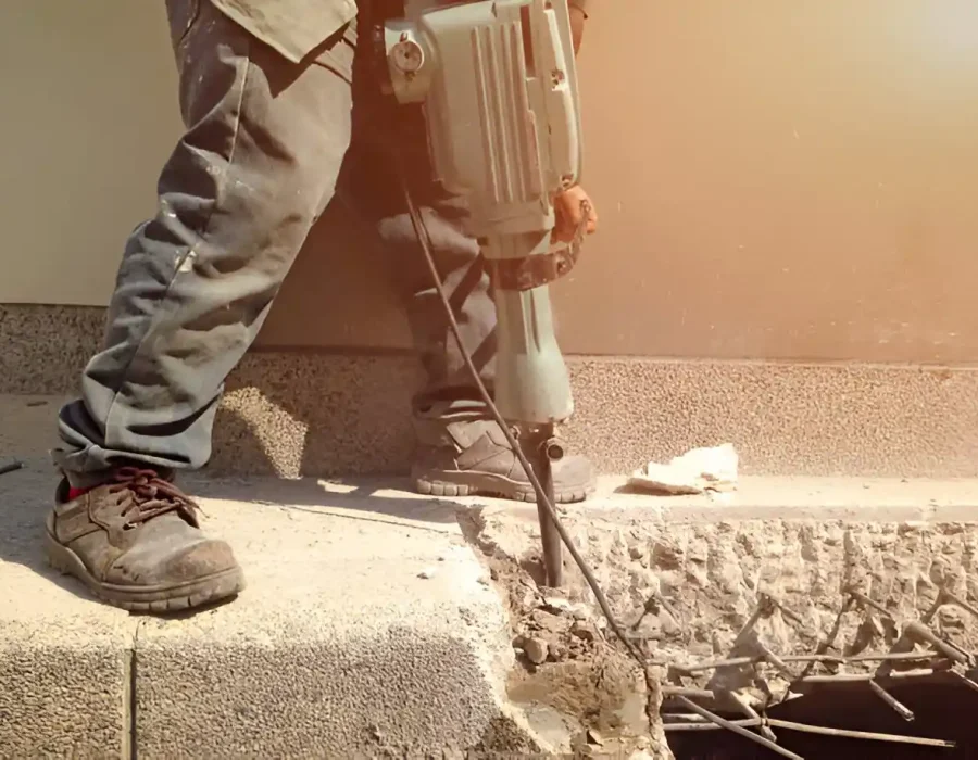 Construction worker breaking concrete with a jackhammer for demolition and site preparation.