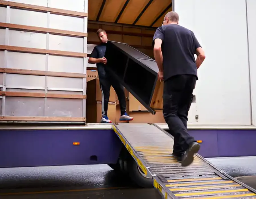 Moving crew loading large furniture onto truck using loading ramp for professional removal and disposal services