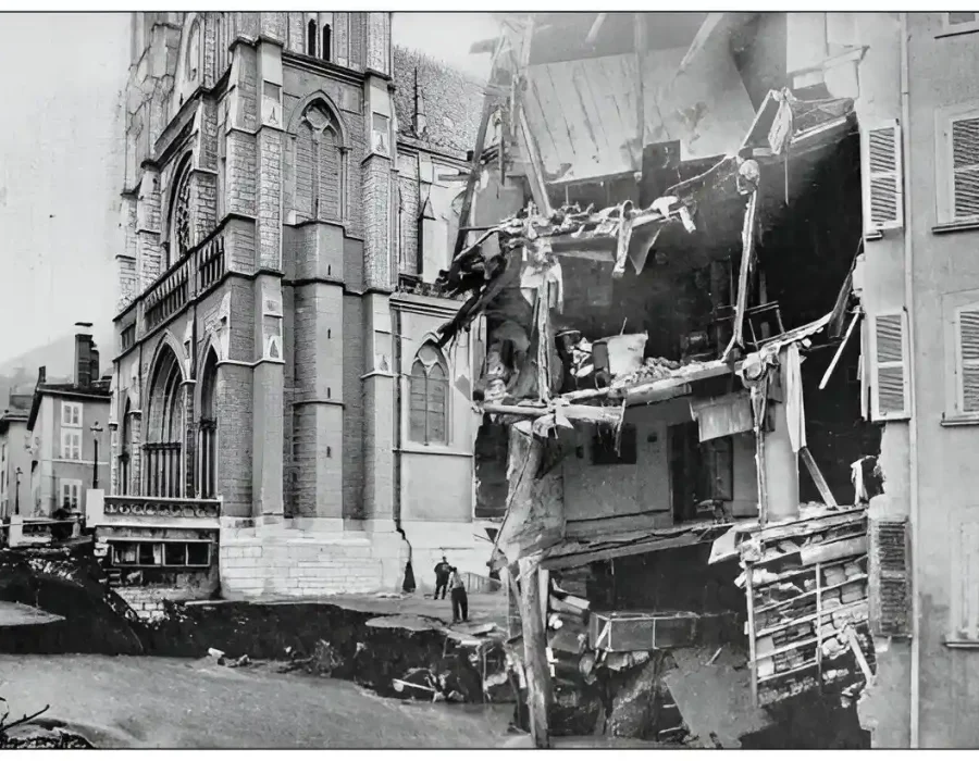 Severely damaged building next to a historic church after partial collapse. Debris visible on-site.