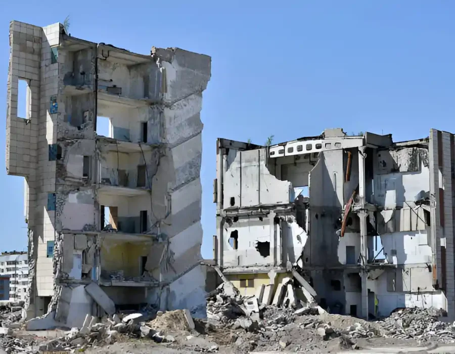 Partially demolished concrete building surrounded by rubble under a clear blue sky.