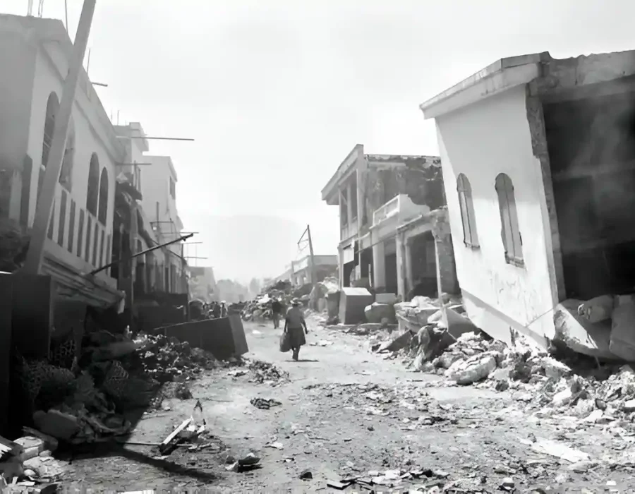 Street lined with earthquake-damaged buildings and scattered debris requiring urgent cleanup and removal services