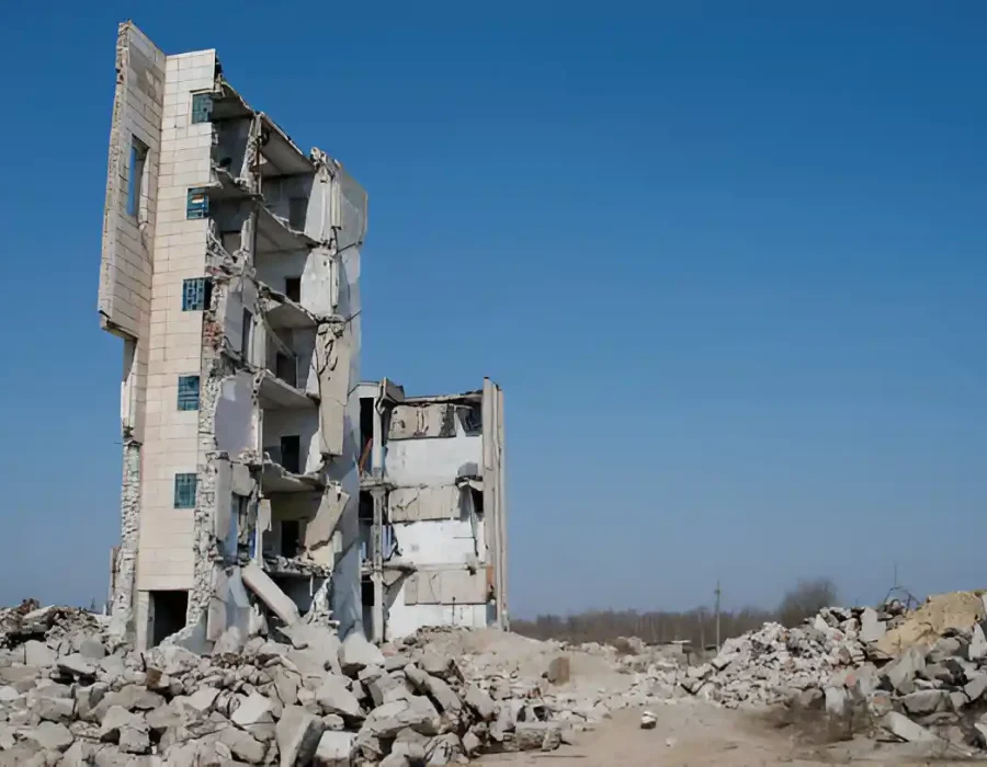 A half-demolished building surrounded by piles of rubble under a clear blue sky.