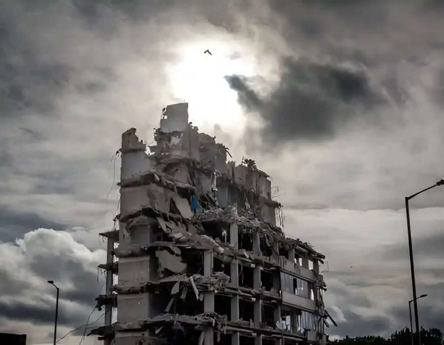 A partially demolished building with debris under a dramatic cloudy sky and sunlight breaking through.