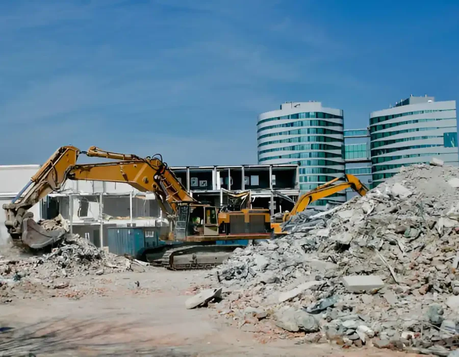 Excavators dismantling commercial building with modern office towers in background