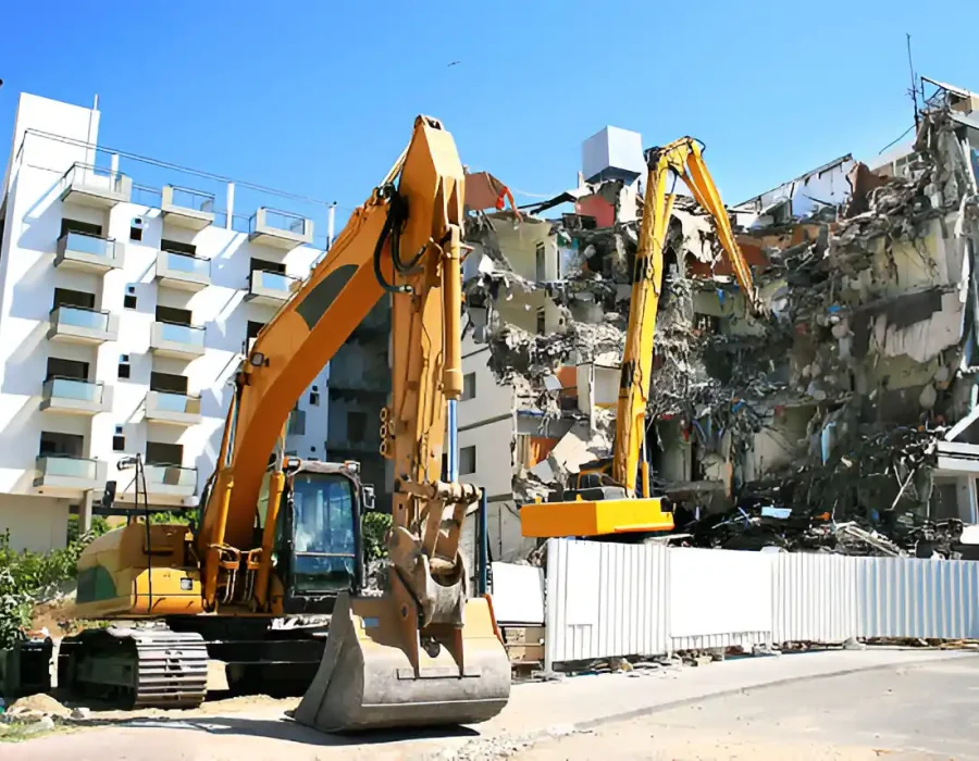 Yellow excavators dismantling multi-story residential building with white fence perimeter