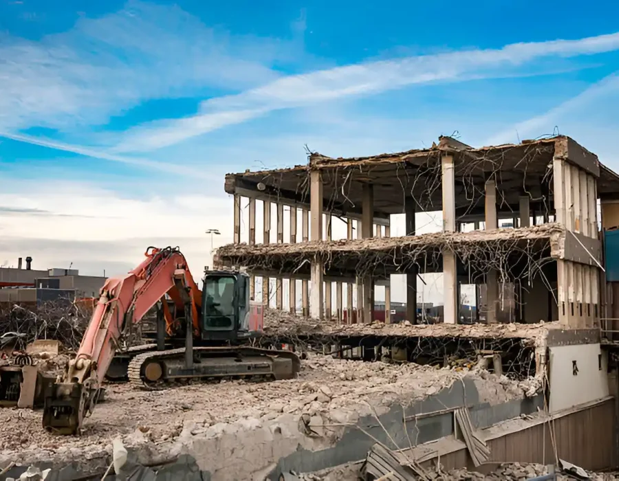 Red excavator dismantling multi-story concrete structure with exposed columns