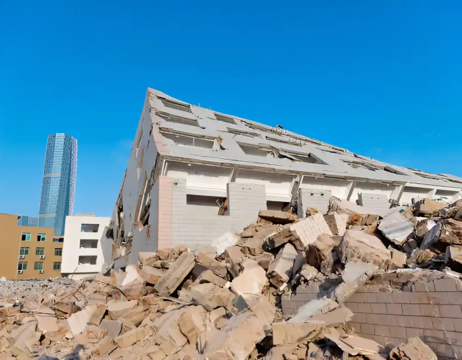 Collapsed white building with massive concrete debris and skyscraper in background