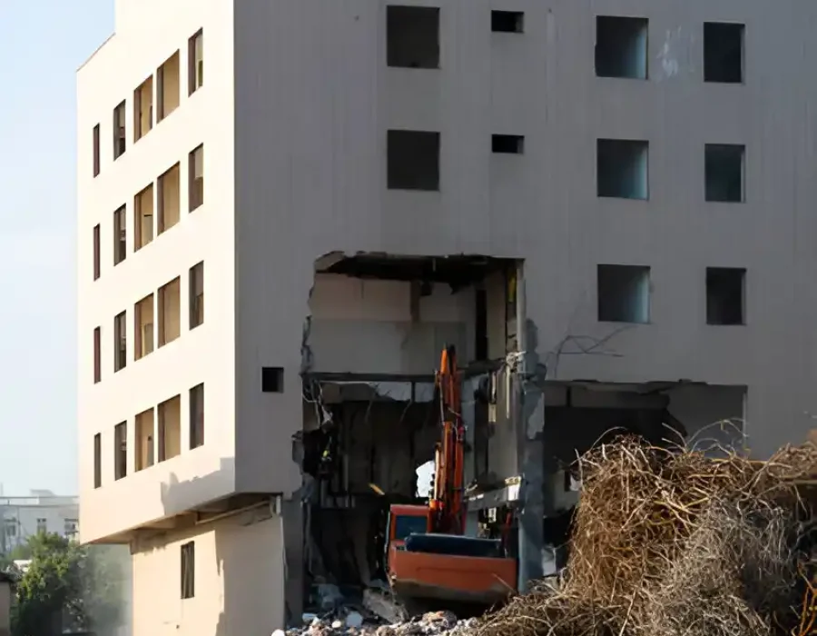 Excavator Dismantling White Concrete Building with Debris Surrounding