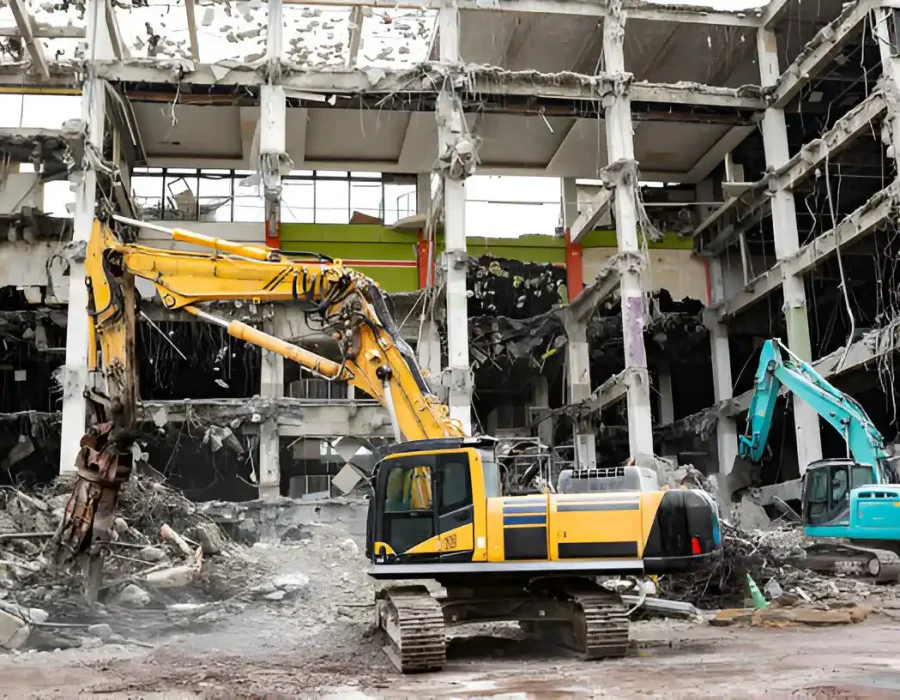 Multiple excavators demolishing building interior with exposed concrete columns and debris cleanup