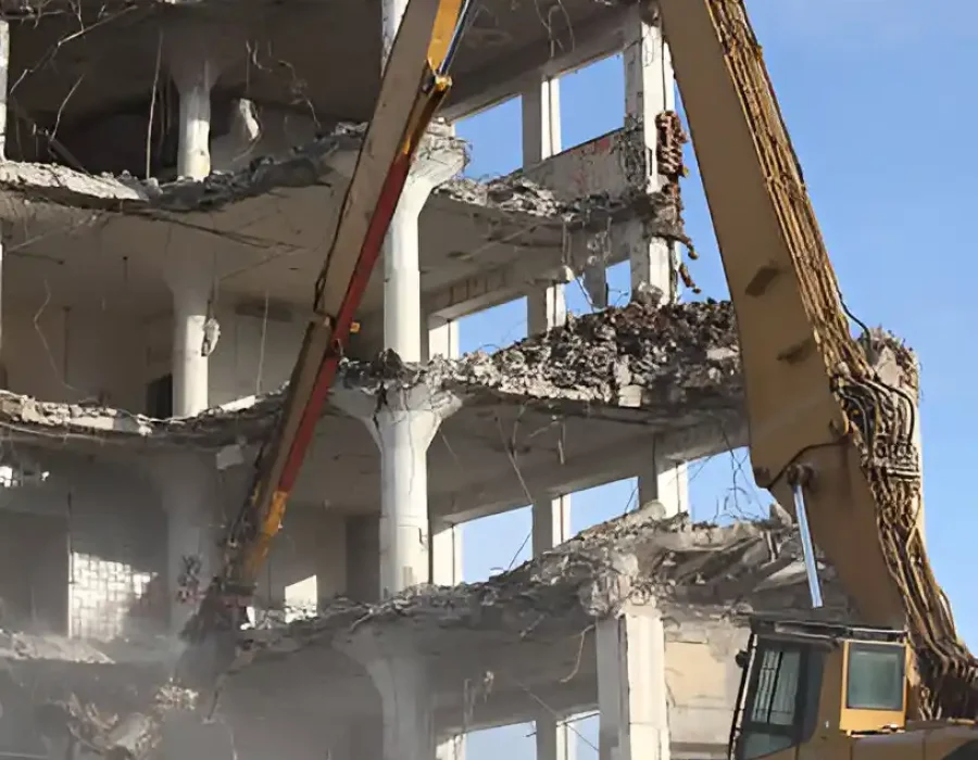 Long-arm excavator systematically dismantling multi-story concrete building structure