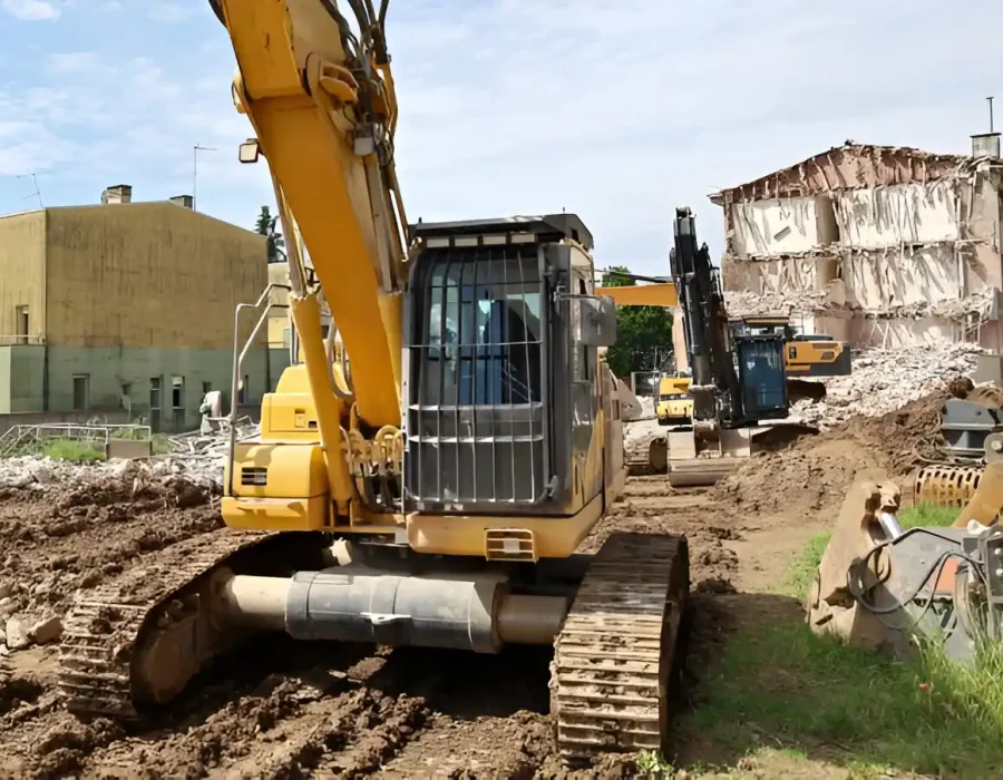 Yellow excavator preparing site with demolished building in background