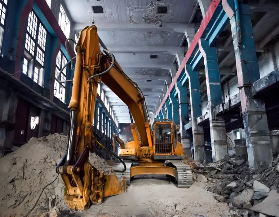 Gray excavator crushing concrete rubble, construction site with safety barriers