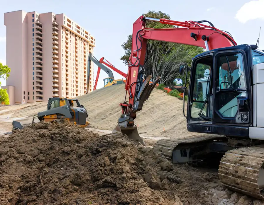 Red and yellow excavators moving earth near high-rise building, site preparation