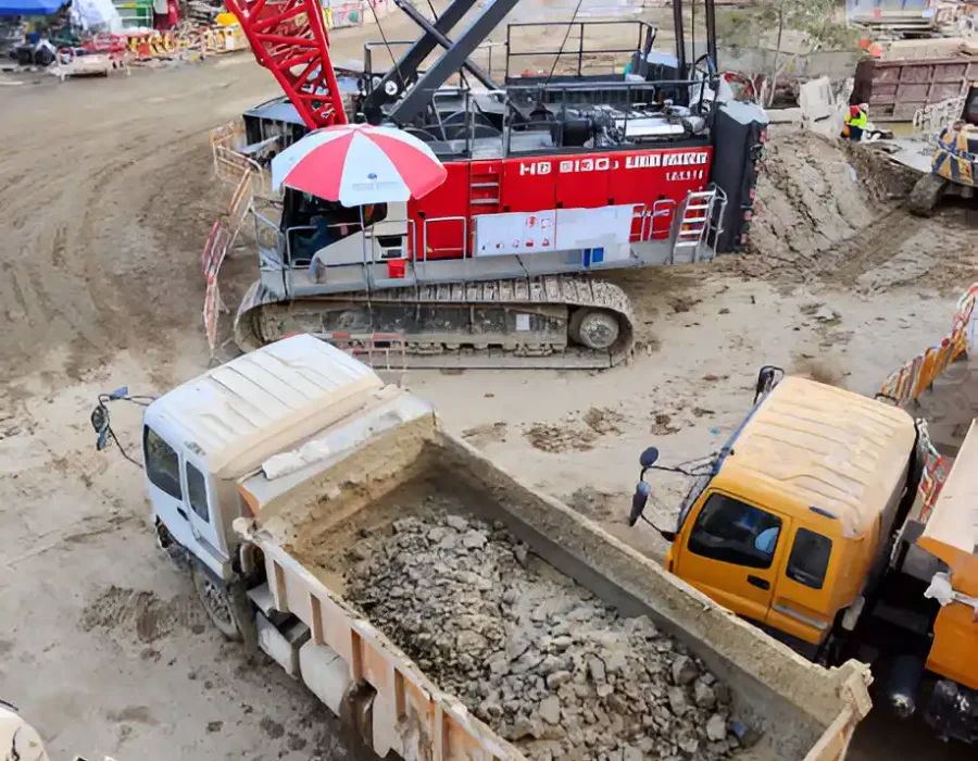 Crawler crane and dump trucks managing concrete debris removal at urban construction site