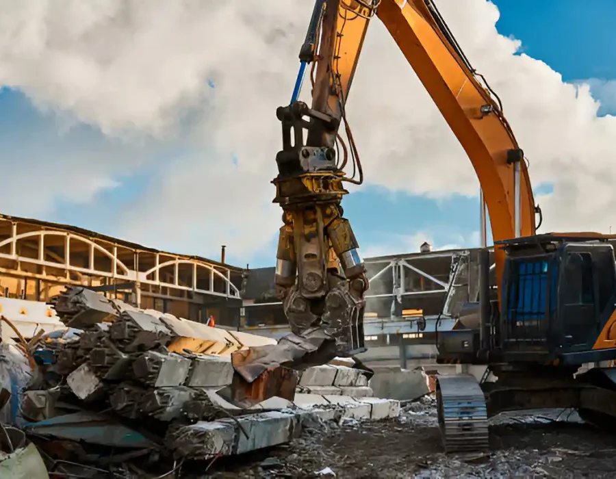Yellow excavator with grapple sorting demolished concrete at industrial site