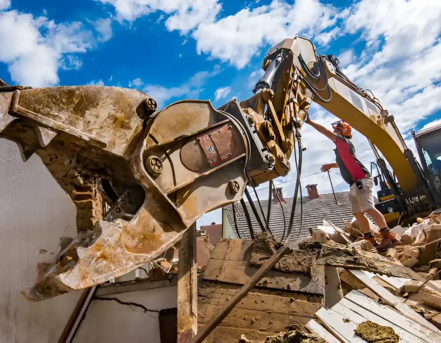 Hydraulic demolition tool crushing building materials, worker near yellow excavator