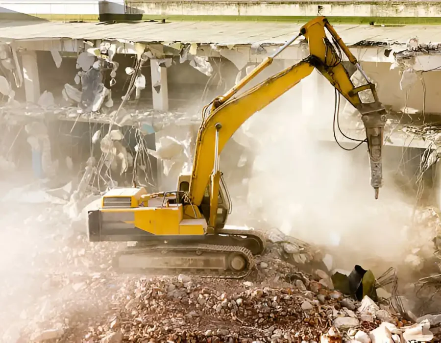 Yellow excavator demolishing concrete building, dust and debris in urban demolition site