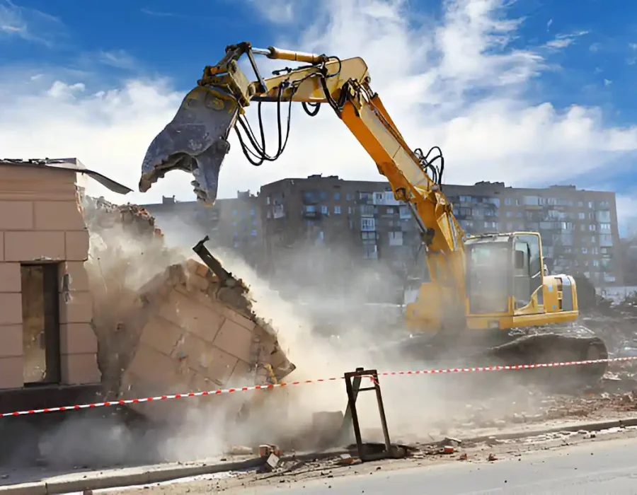 Yellow excavator breaking down building with dust and debris in city setting